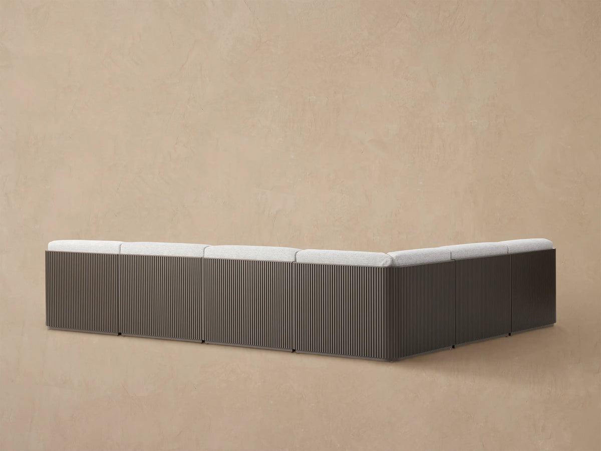 Close-up Beaumont Outdoor Sectional corner: dark brown slatted aluminum frame, light gray textured seat & back cushions.