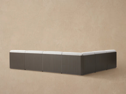 Close-up Beaumont Outdoor Sectional corner: dark brown slatted aluminum frame, light gray textured seat & back cushions.
