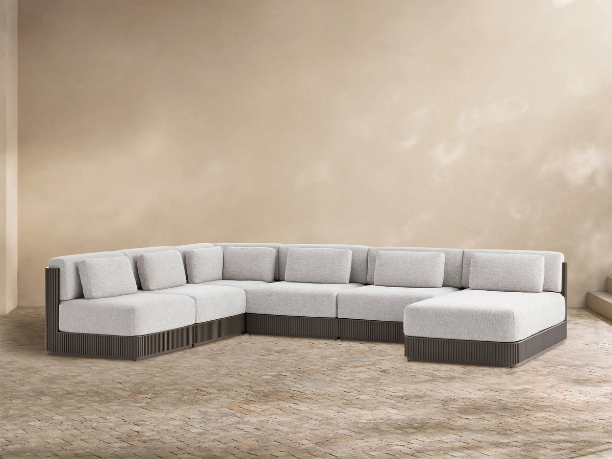 Beaumont Outdoor Aluminum Six-Piece Sectional with Chaise. Light grey cushions, dark brown slatted base on a brick patio.