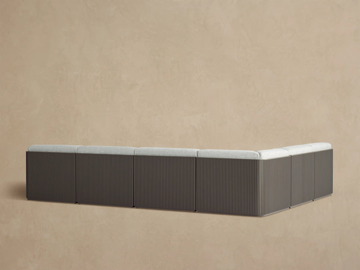 Angled view of Beaumont Outdoor Sectional with light gray textured cushions on a dark bronze slatted aluminum frame.