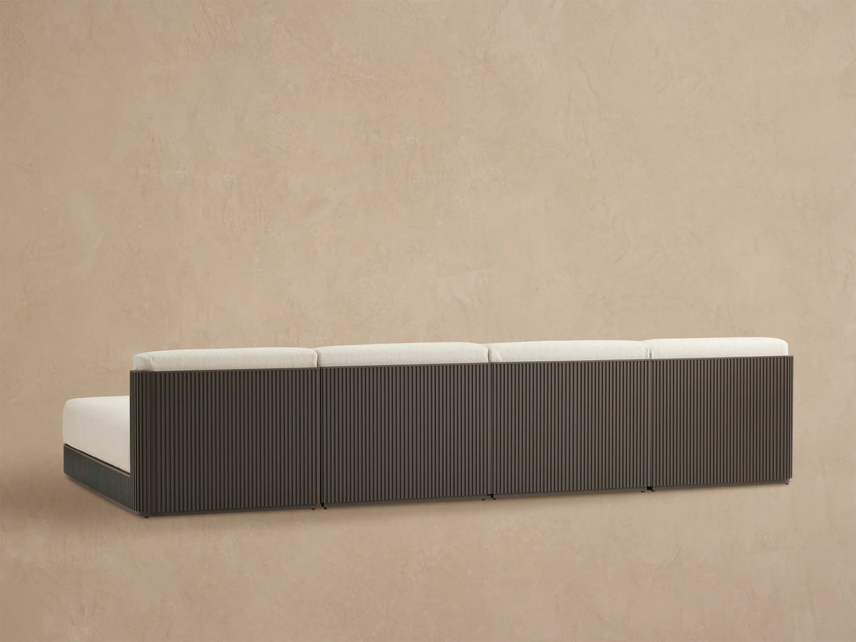 Close-up of Beaumont sectional's dark gray slatted aluminum frame and light beige textured cushions, viewed from above.