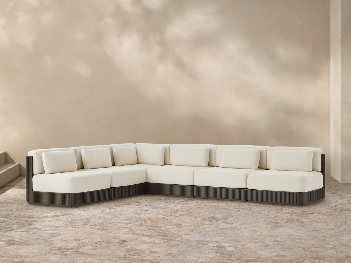 Beaumont Outdoor Aluminum Six-Piece Sectional. L-shaped, with cream cushions & dark slatted aluminum base on a tiled patio.