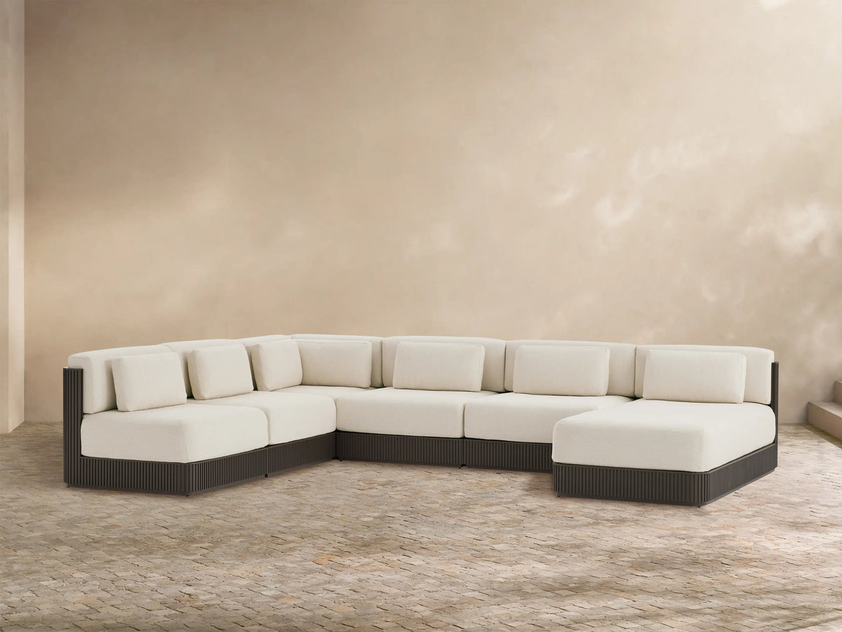 Beaumont 6-pc U-shaped outdoor sectional with right chaise. Cream cushions, dark ribbed base, on a stone patio with beige wall.