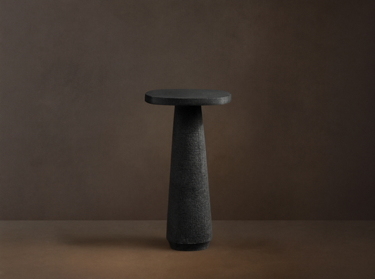 Bellagio Outdoor End Table: Dark gray, textured, with an oval top and tapered column base, on a stone patio against a light wall.