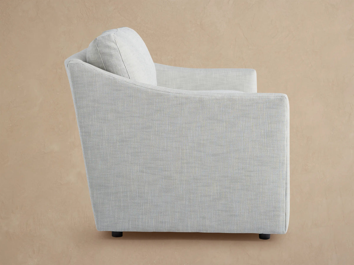 Back view of the light grey Branson Outdoor Sofa, upholstered in fabric, with two loose back cushions, against a tan wall.