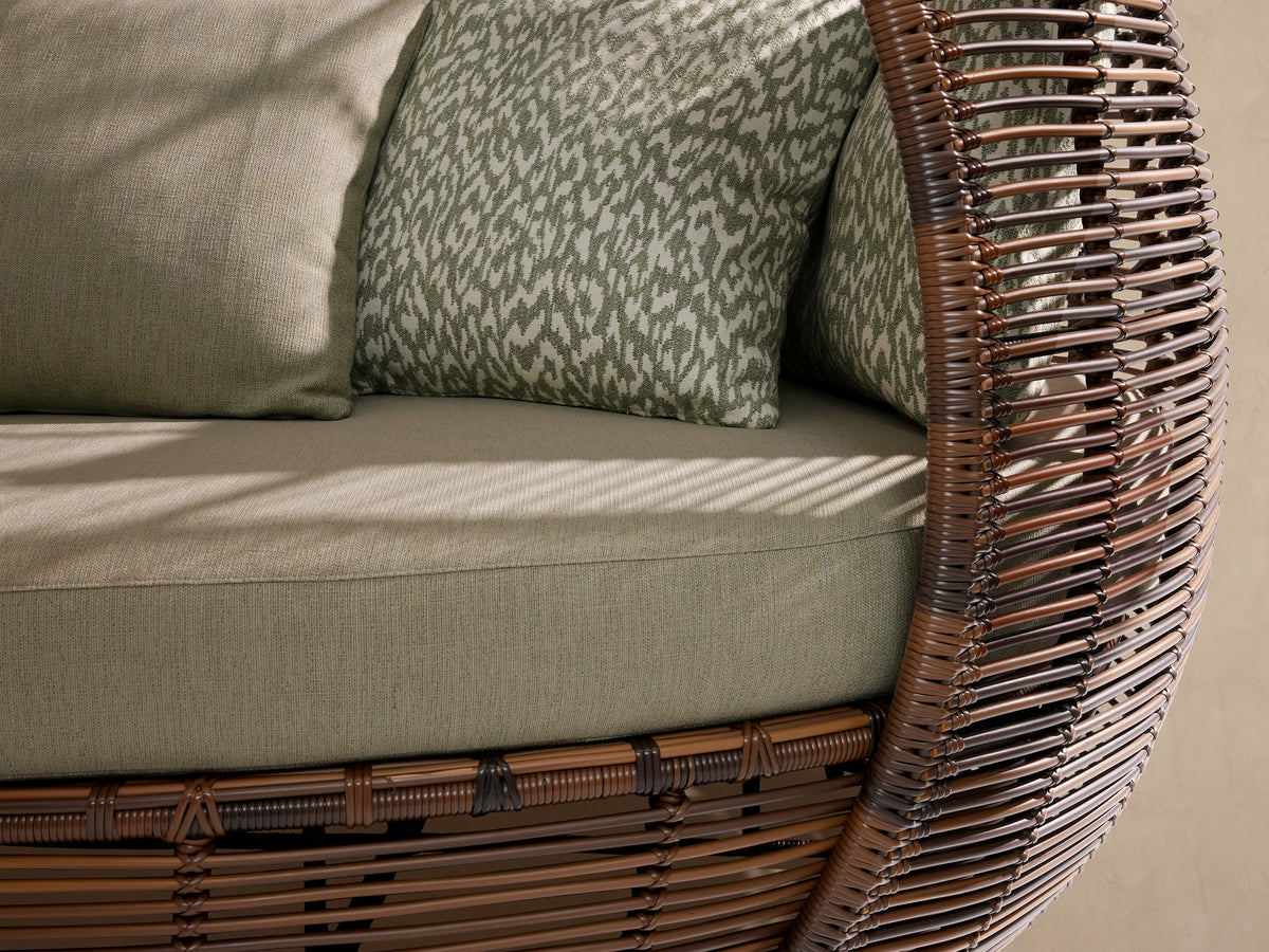 Calusa Outdoor Daybed, dark brown handwoven wicker with an egg-shaped canopy, light green cushions & patterned pillows.