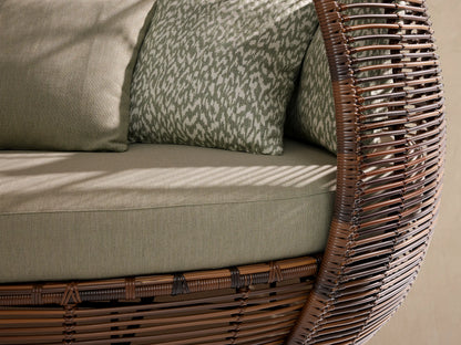 Calusa Outdoor Daybed, dark brown handwoven wicker with an egg-shaped canopy, light green cushions & patterned pillows.
