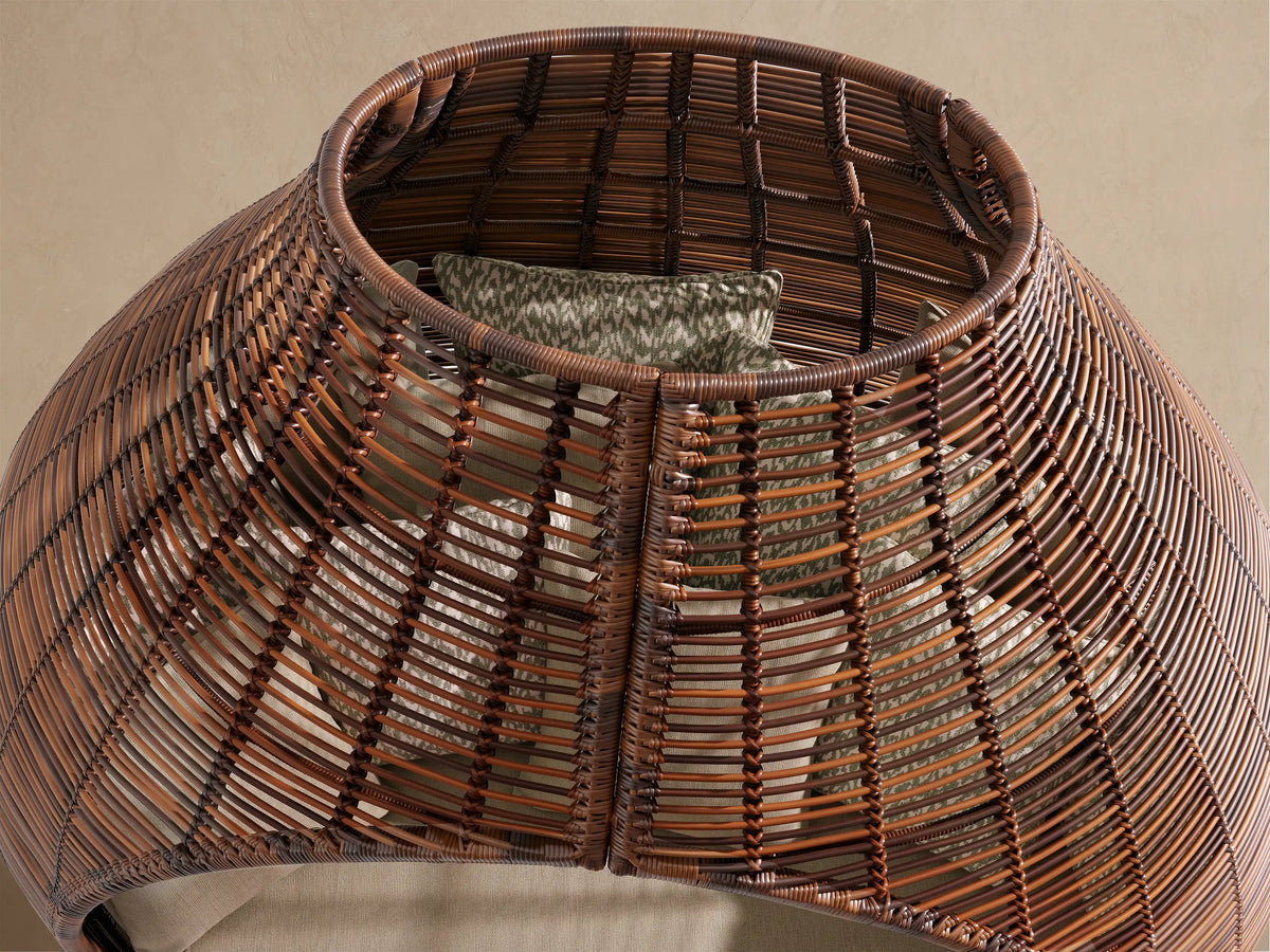 Close-up of Calusa Outdoor Daybed in Eden Sage, showing dark brown wicker, deep sage cushion, and patterned pillow with dappled shadows.