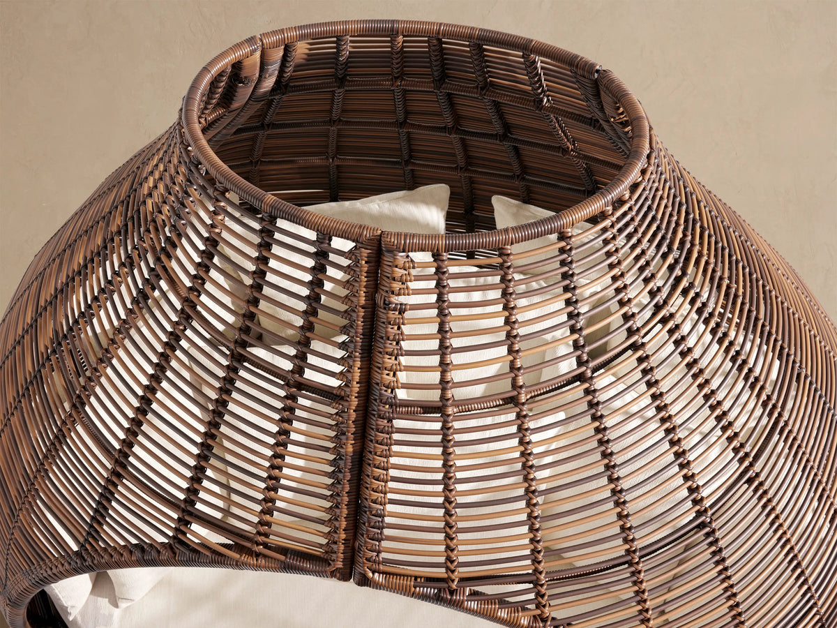 Close-up of the intricate brown handwoven all-weather wicker on the Calusa Outdoor Daybed, with light toss pillows visible inside.