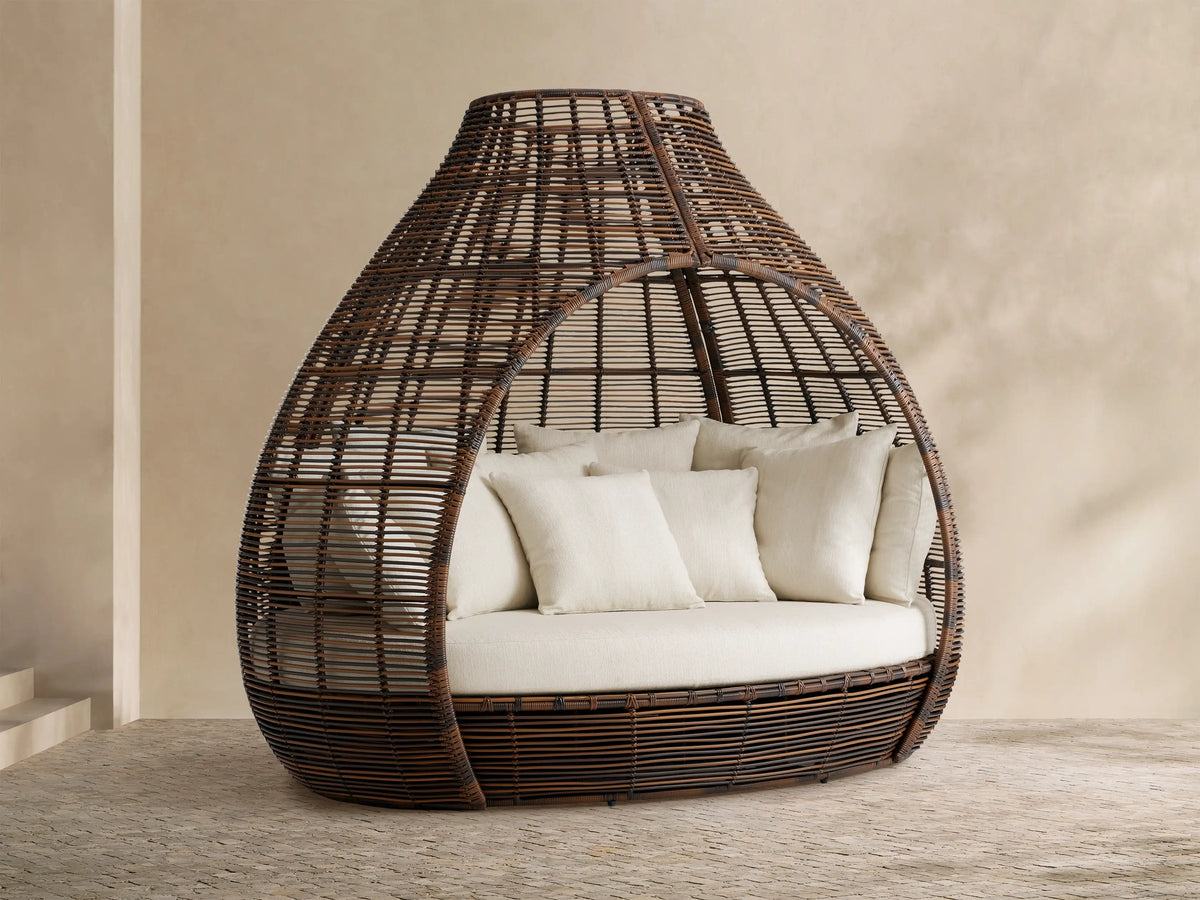 Front view of the brown handwoven Calusa Outdoor Daybed with a cream seat cushion and toss pillows inside.