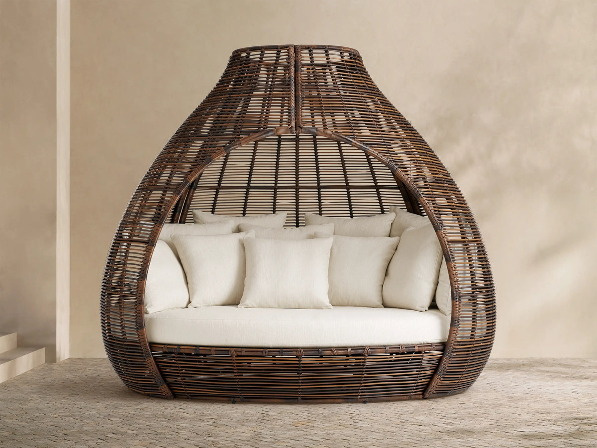Light grey Calusa Outdoor Collection Cover draped over a round outdoor furniture piece on a paved patio against a tan wall.