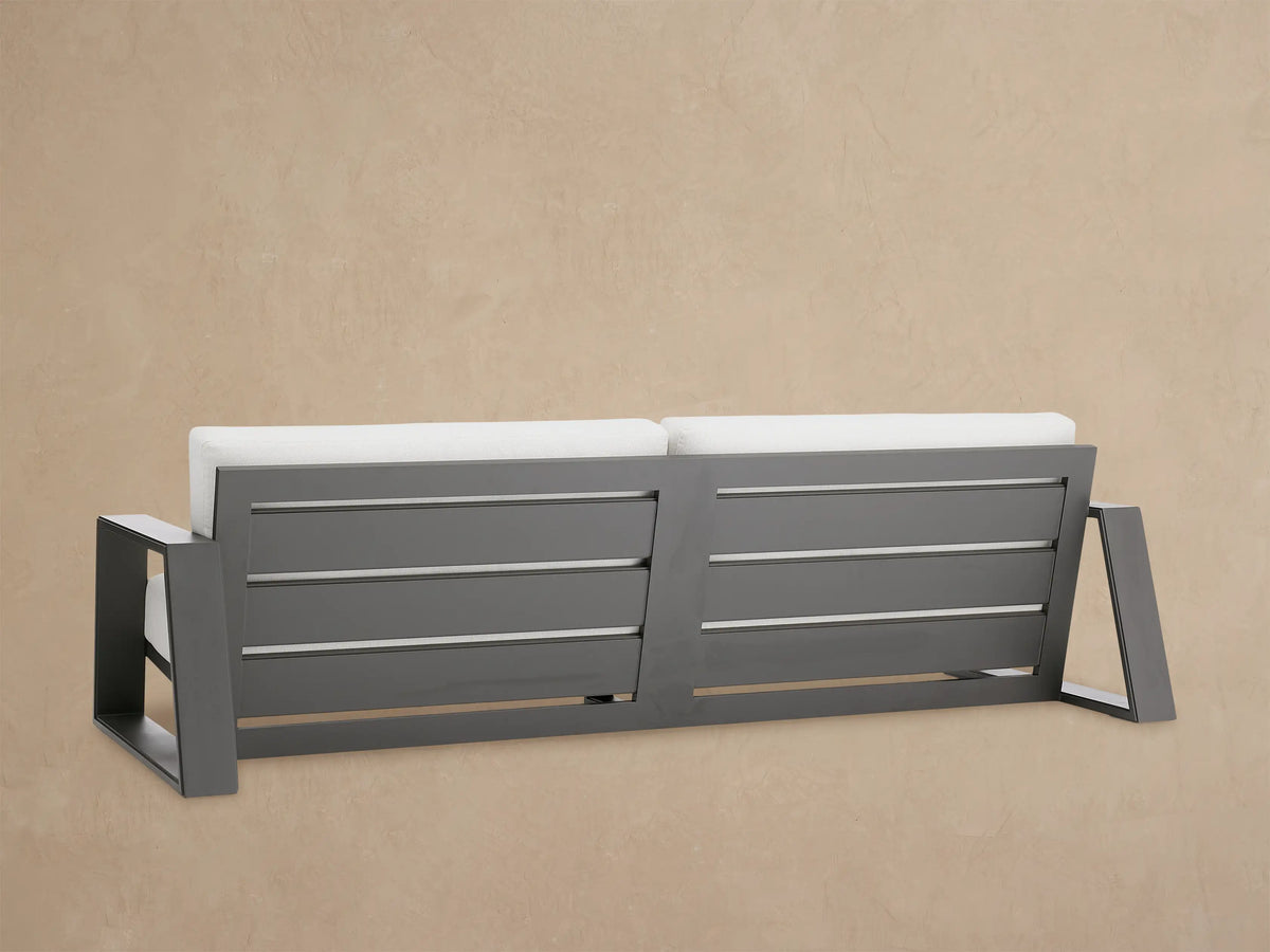 Canyon Outdoor Aluminum Sofa, close-up. Dark matte gray aluminum frame with rectangular armrest and light gray cushions.