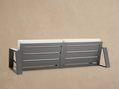 Canyon Outdoor Aluminum Sofa, close-up. Dark matte gray aluminum frame with rectangular armrest and light gray cushions.