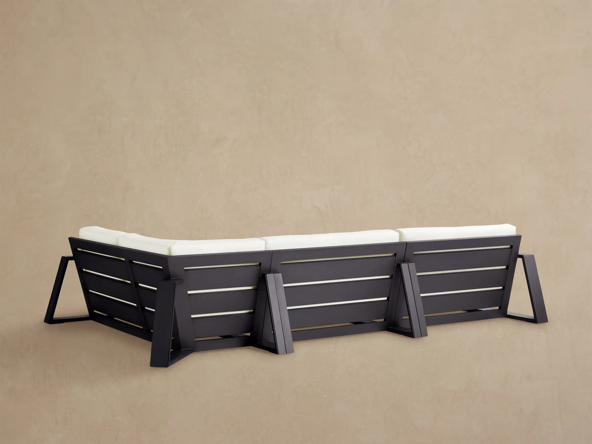 Canyon Outdoor Sectional, close-up of corner. White seat & back cushions, dark gray aluminum frame on tan surface.