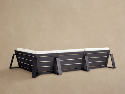 Canyon Outdoor Sectional, close-up of corner. White seat & back cushions, dark gray aluminum frame on tan surface.