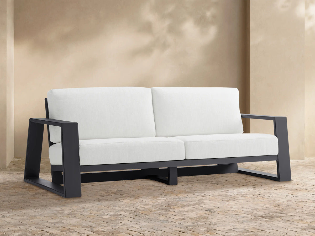Canyon Outdoor Aluminum Sofa: 2-seater, dark gray aluminum frame, white cushions, viewed straight on against a light tan wall.