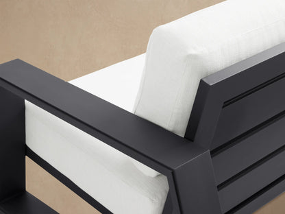 Canyon Outdoor Aluminum Sofa, two-seater, with a sleek dark gray frame & thick white cushions, on a patio with a light wall.