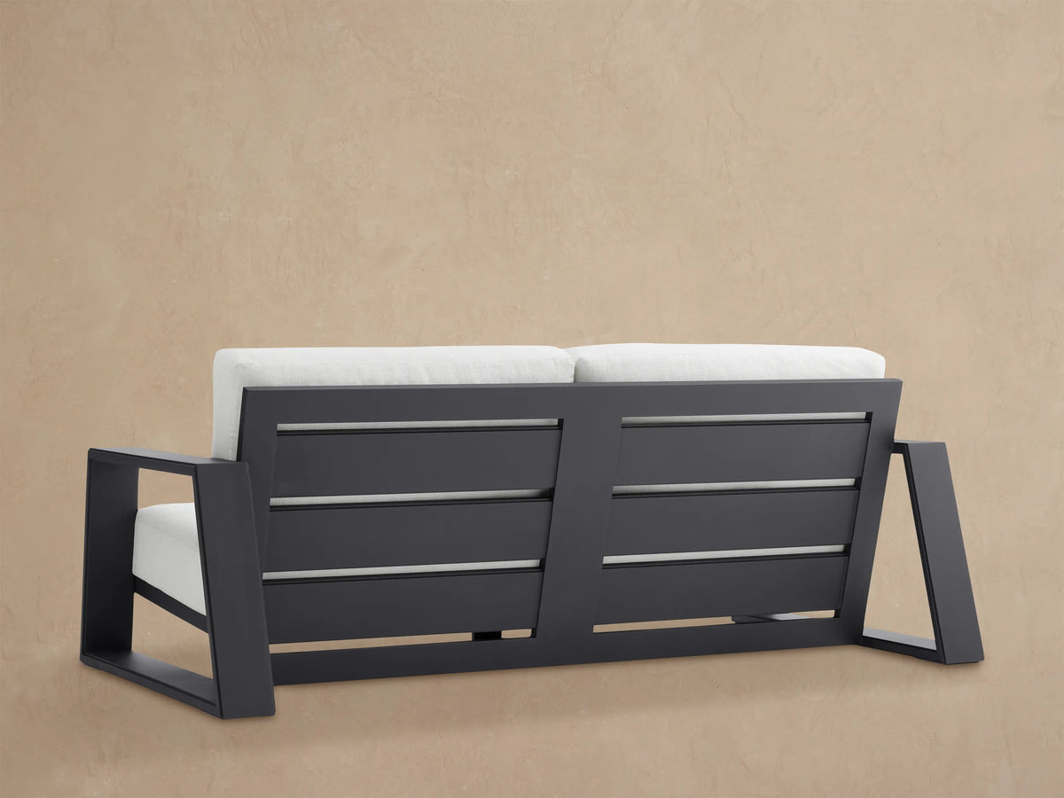 Close-up, angled view of Canyon Outdoor Aluminum Sofa. Dark gray frame with clean, angular lines & thick white cushions.