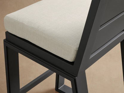 Canyon Outdoor Aluminum Barstool, dark gray frame, two horizontal back slats, light beige cushion, on tiled floor.