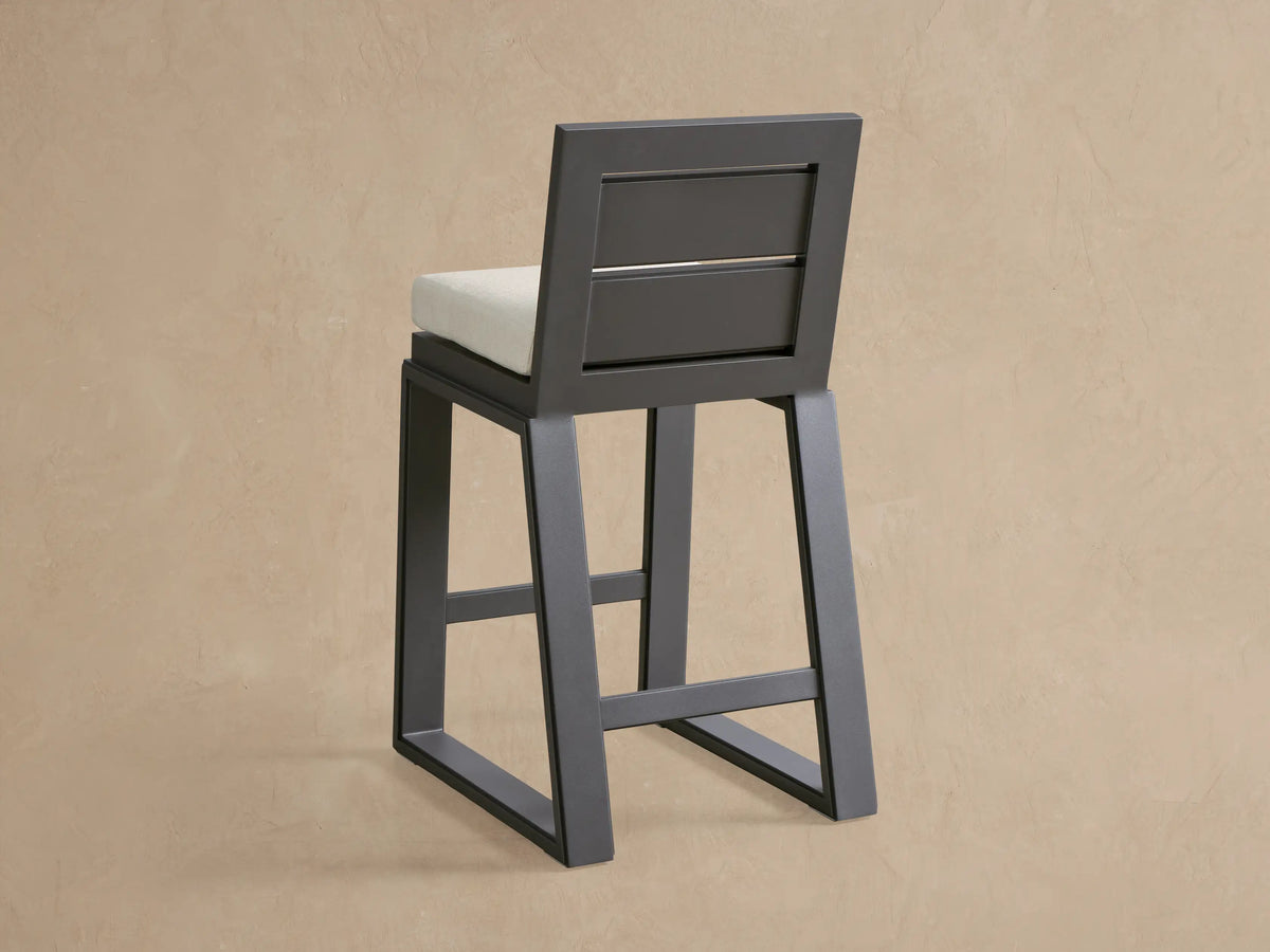 Close-up of a Canyon Outdoor Aluminum Barstool's dark gray frame and light beige textured seat cushion.