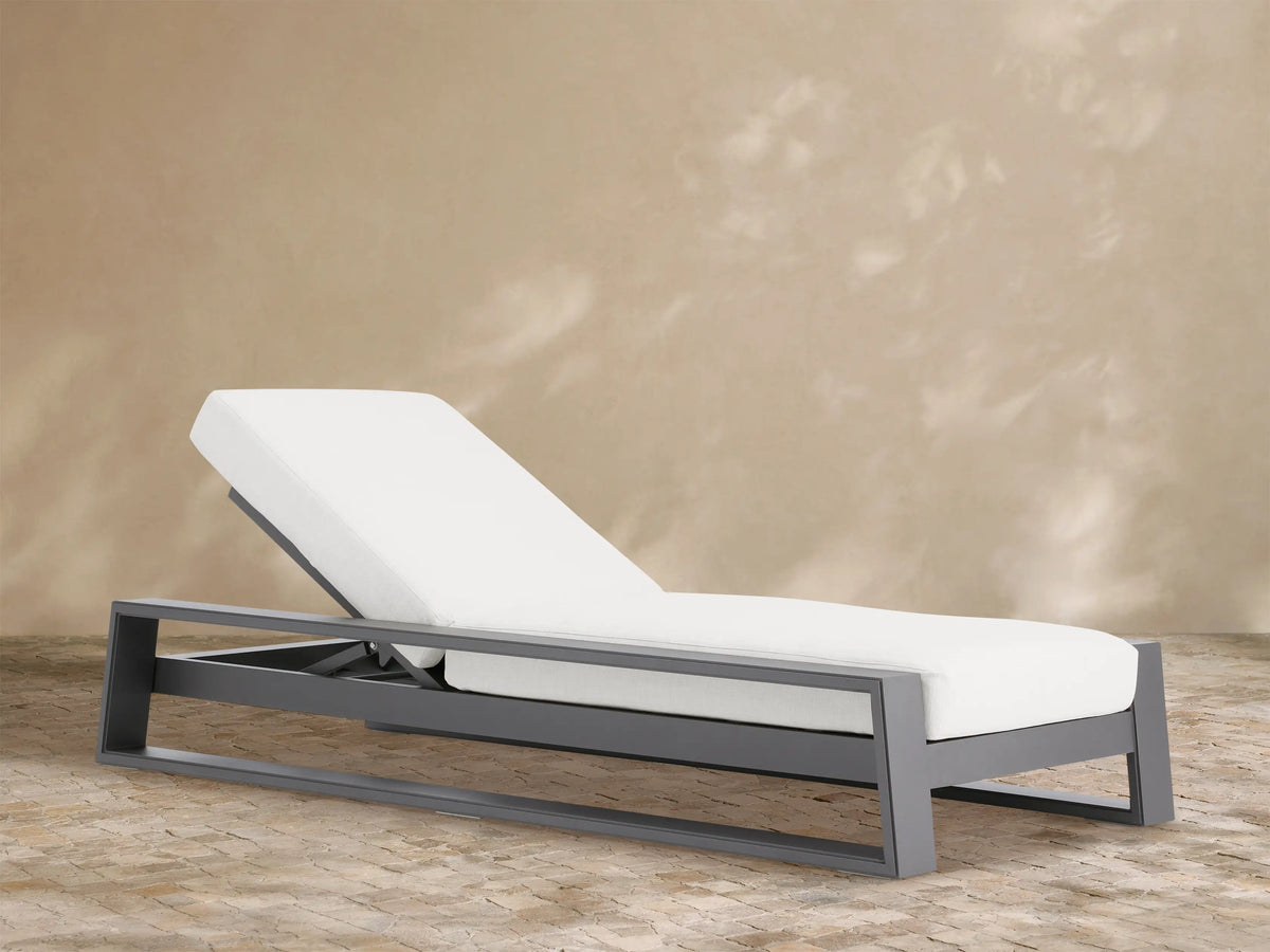 Canyon Outdoor Aluminum Chaise with dark gray frame and white cushions, backrest elevated, angled view on light brown patio.