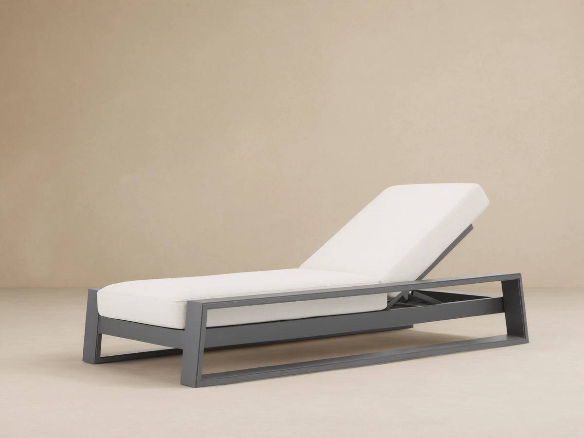 Canyon Outdoor Aluminum Chaise with dark gray frame and white cushions, backrest elevated, angled view on light brown patio.