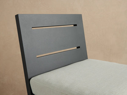Dark gray Canyon Outdoor Aluminum Counter Stool with slatted back and light cream cushion, in an outdoor setting on a stone patio.