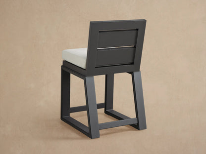 Canyon Outdoor Aluminum Counter Stool's dark gray back with two slots, angled above its light gray textured cushion.