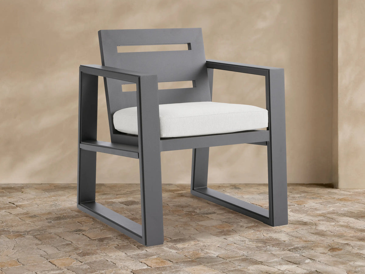 Canyon aluminum dining arm chair, dark gray geometric frame, two horizontal back slats, white seat cushion on stone patio.