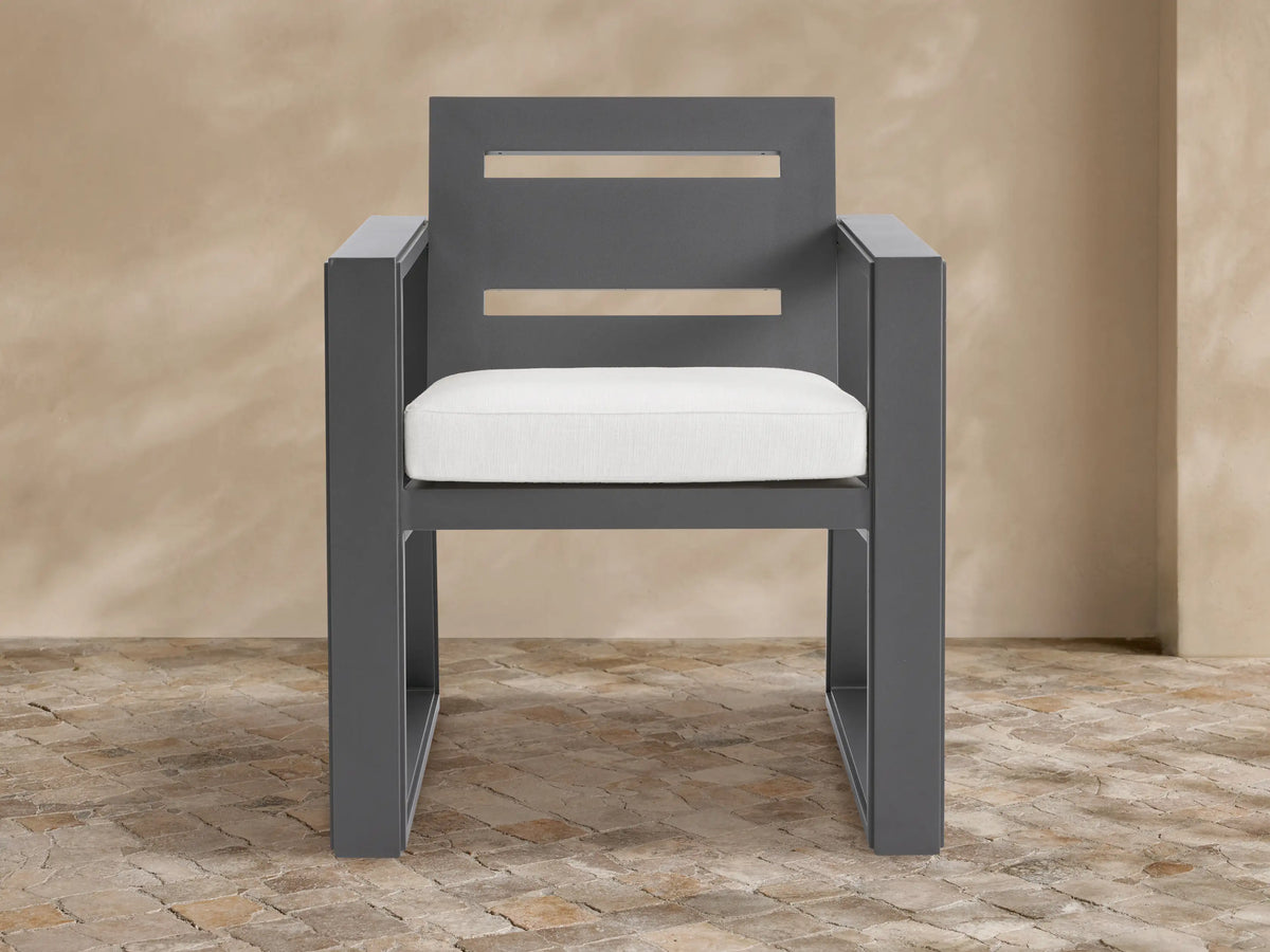 Canyon aluminum dining arm chair, dark gray geometric frame, two horizontal back slats, white seat cushion on stone patio.