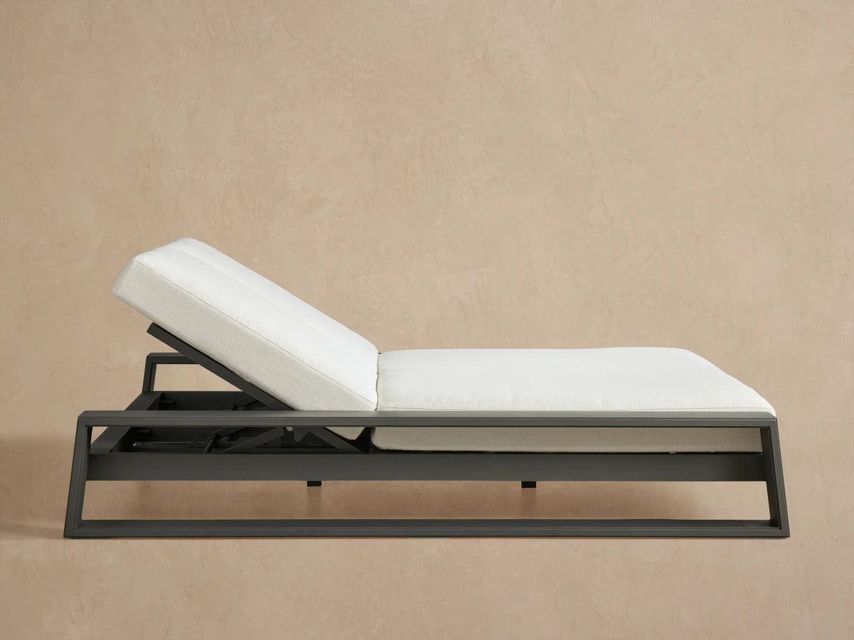 Canyon Outdoor Aluminum Double Chaise with a charcoal frame & two white cushions, both backrests angled up, on a patio.