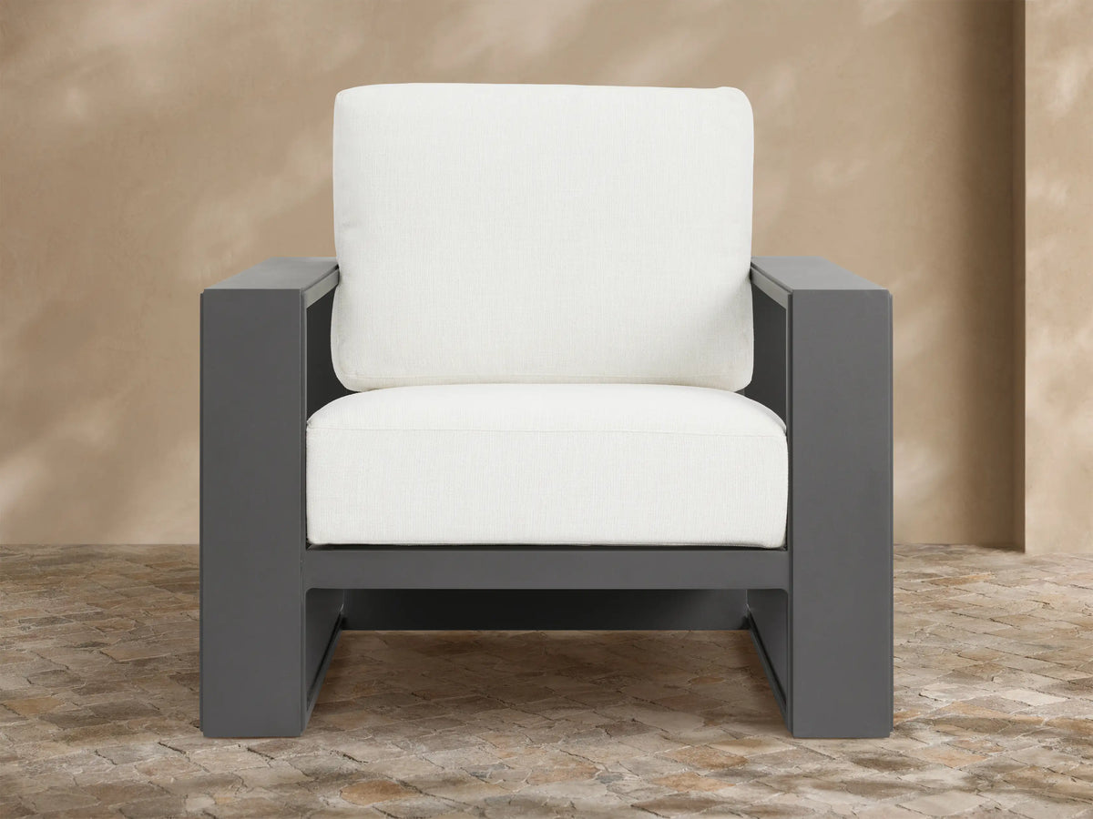 Canyon Outdoor Aluminum Lounge Chair with a dark gray angular aluminum frame and thick white cushions, angled on a stone patio.