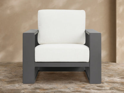 Canyon Outdoor Aluminum Lounge Chair with a dark gray angular aluminum frame and thick white cushions, angled on a stone patio.