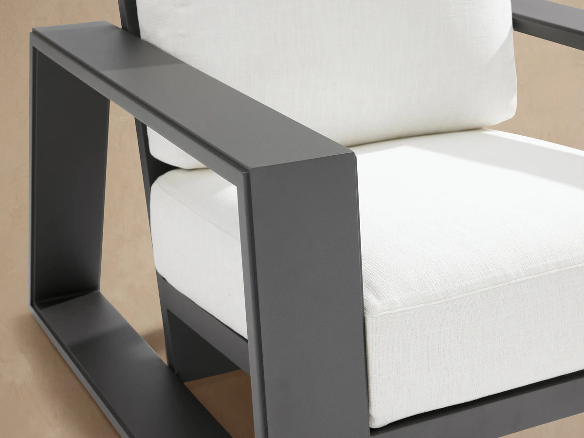 Dark gray Canyon outdoor aluminum lounge chair with thick off-white seat & back cushions, seen from front on stone patio.