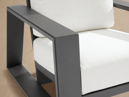 Dark gray Canyon outdoor aluminum lounge chair with thick off-white seat & back cushions, seen from front on stone patio.