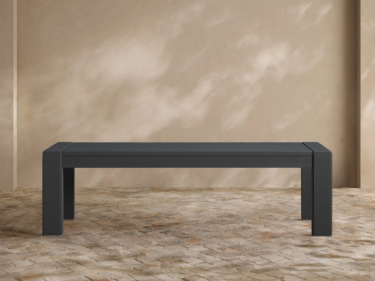 Dark gray Canyon Outdoor Aluminum Dining Bench, modern rectangular design, on a tiled patio against a tan wall.