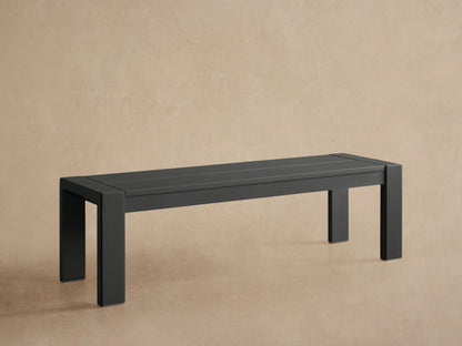 Dark gray Canyon Outdoor Aluminum Dining Bench, modern rectangular design, on a tiled patio against a tan wall.