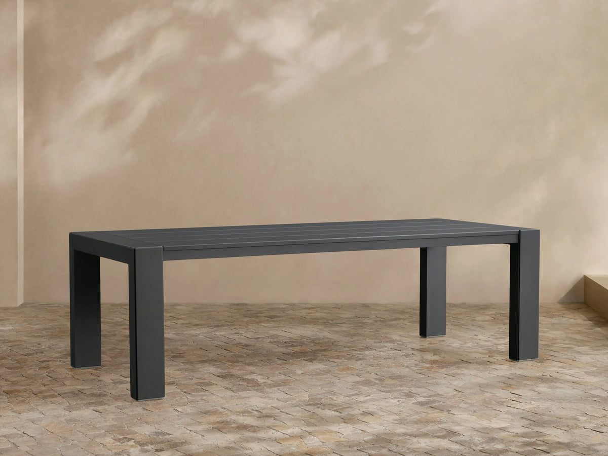 Canyon Outdoor Aluminum Dining Table. A long, rectangular, dark gray table with sturdy legs on an outdoor paved patio.
