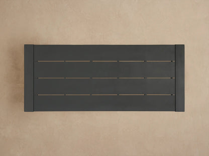 Dark gray Canyon Outdoor Aluminum Dining Table corner, showing a slatted top and thick square leg on a brown background.