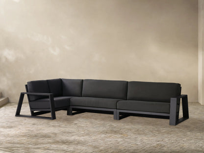 Canyon Outdoor Aluminum Three-Piece Sectional, L-shaped, with black cushions and dark gray aluminum frame against a tan wall.