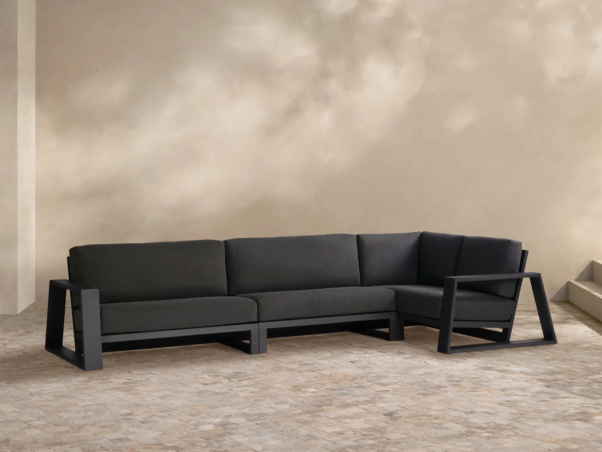 Canyon Outdoor Aluminum Three-Piece Sectional. L-shaped dark gray sofa with sleek aluminum frame on tiled patio.