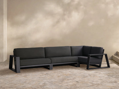 Canyon Outdoor Aluminum Three-Piece Sectional. L-shaped dark gray sofa with sleek aluminum frame on tiled patio.