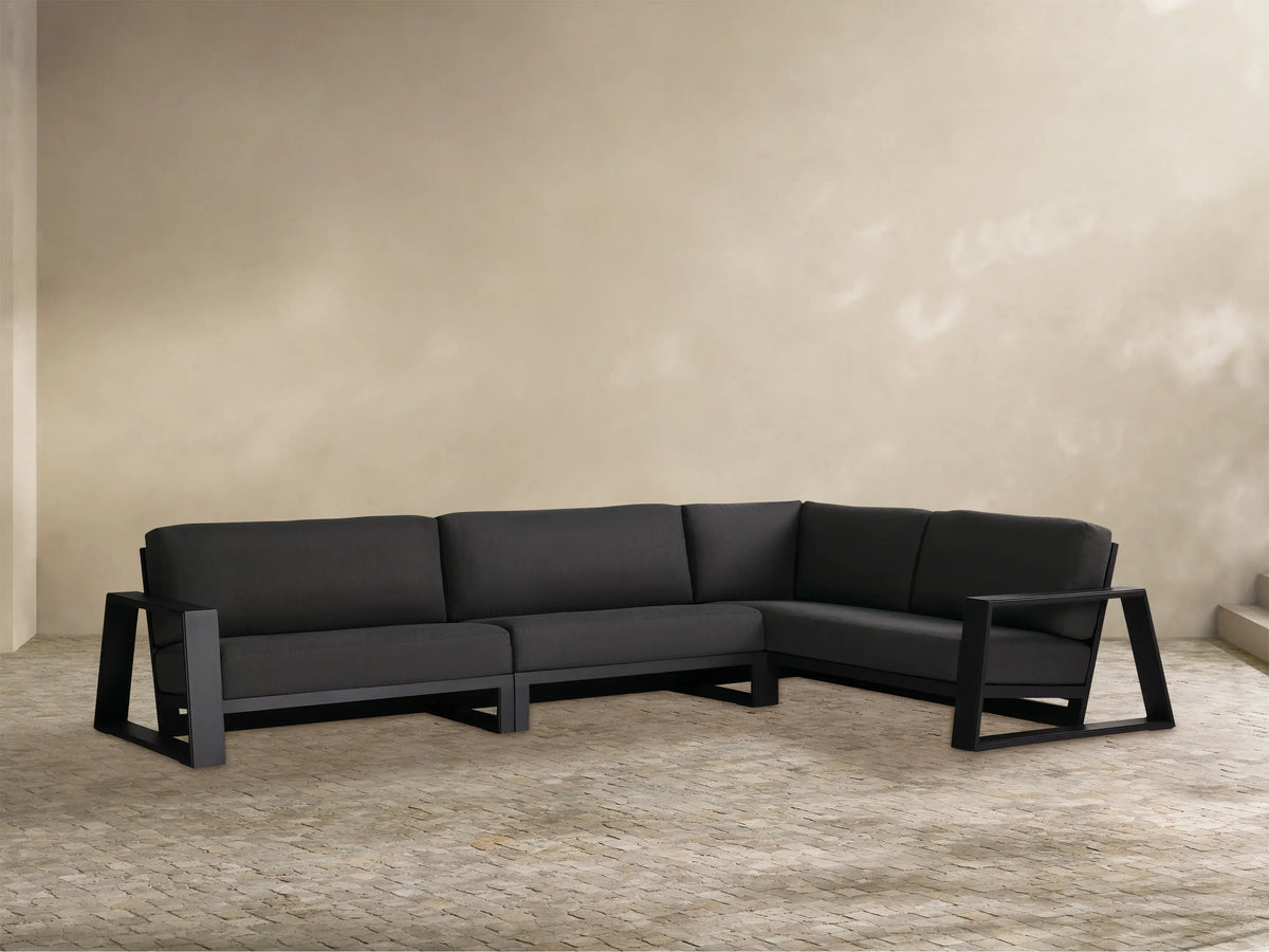 Canyon L-shaped dark gray outdoor sectional, aluminum frame, three pieces. Set on a light patio with a beige wall.