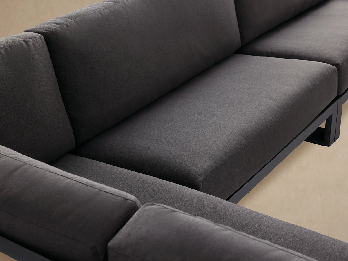 Canyon Outdoor Aluminum Three-Piece Sectional: L-shaped, dark gray cushions, black open frames, on a light paver patio.