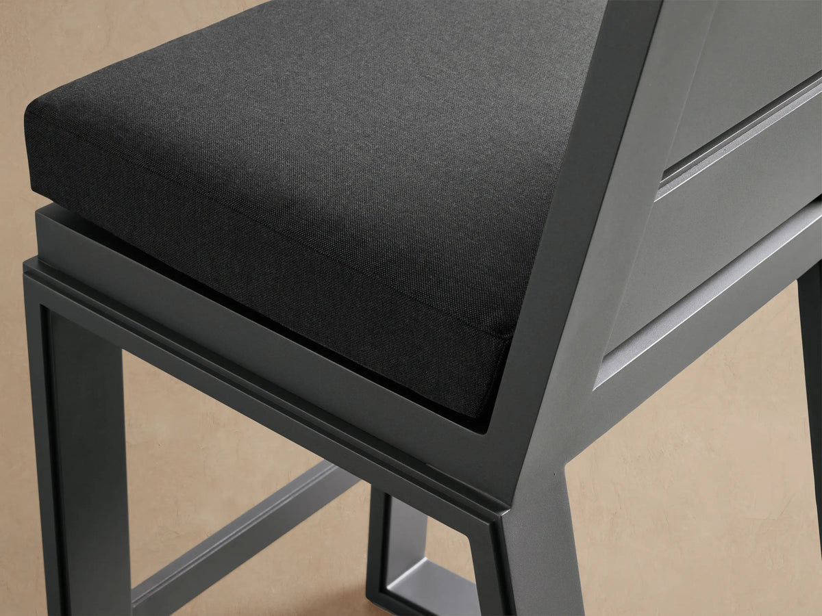 Front view of dark gray Canyon Outdoor Aluminum Barstool with horizontal slatted back and charcoal cushion, on a tiled floor.