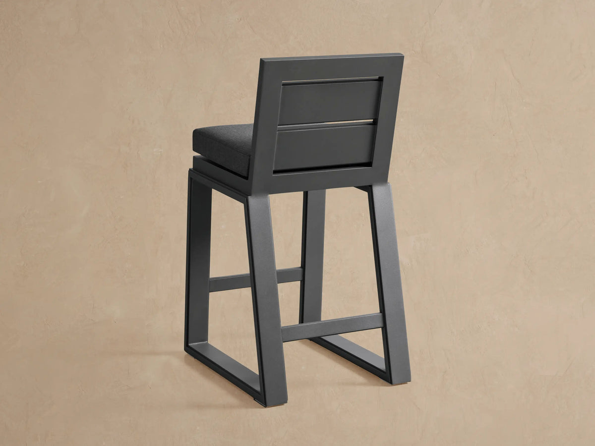 Angled close-up of Canyon Outdoor Aluminum Barstool. Dark gray powder-coated frame and black textured fabric cushion.