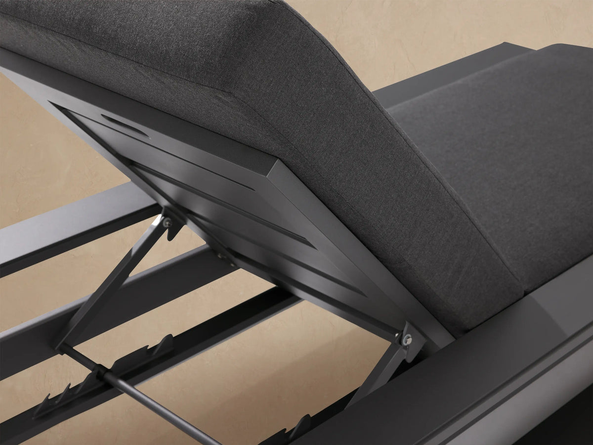 Canyon Outdoor Aluminum Chaise with charcoal gray frame and cushions. Backrest angled up, side view against a beige wall.