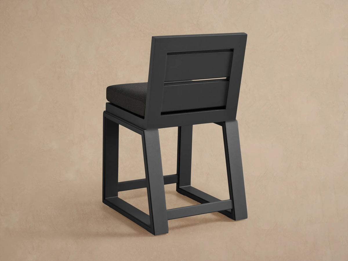 Close-up of Canyon Outdoor Aluminum Counter Stool's dark gray backrest with two horizontal cutouts, and charcoal fabric seat cushion.