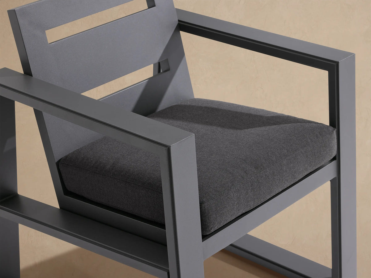 Front view of charcoal gray Canyon Outdoor Aluminum Dining Arm Chair with dark cushion, wide arms, and two horizontal back slots.