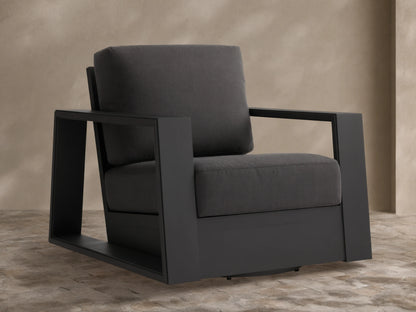 Canyon Outdoor Aluminum Swivel Chair, angled right. Dark charcoal powder-coated frame with thick gray cushions on a stone patio.